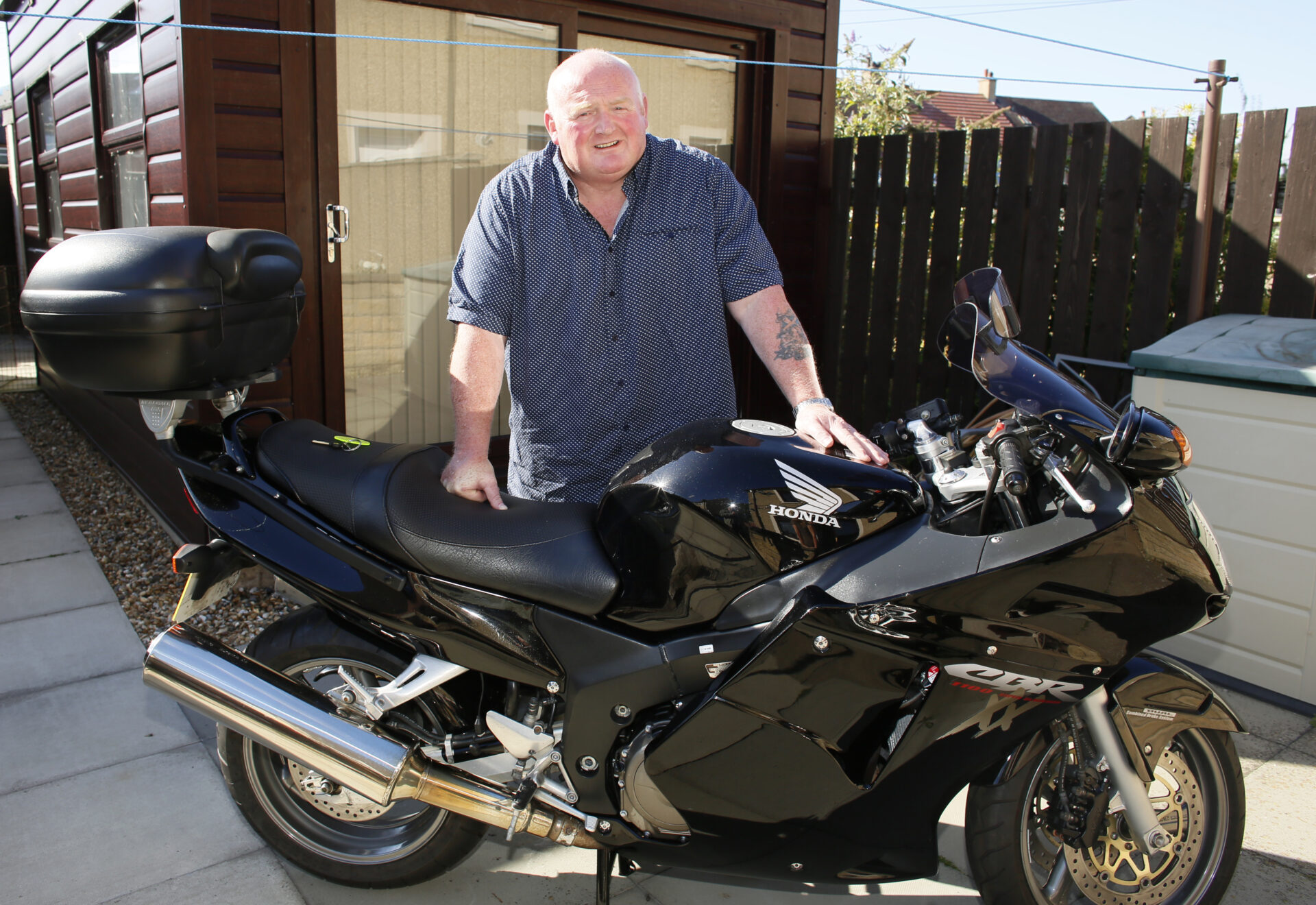 Brian Crawford, a retired refinery worker from Grangemouth, standing outside his home beside his black Honda motorcycle.