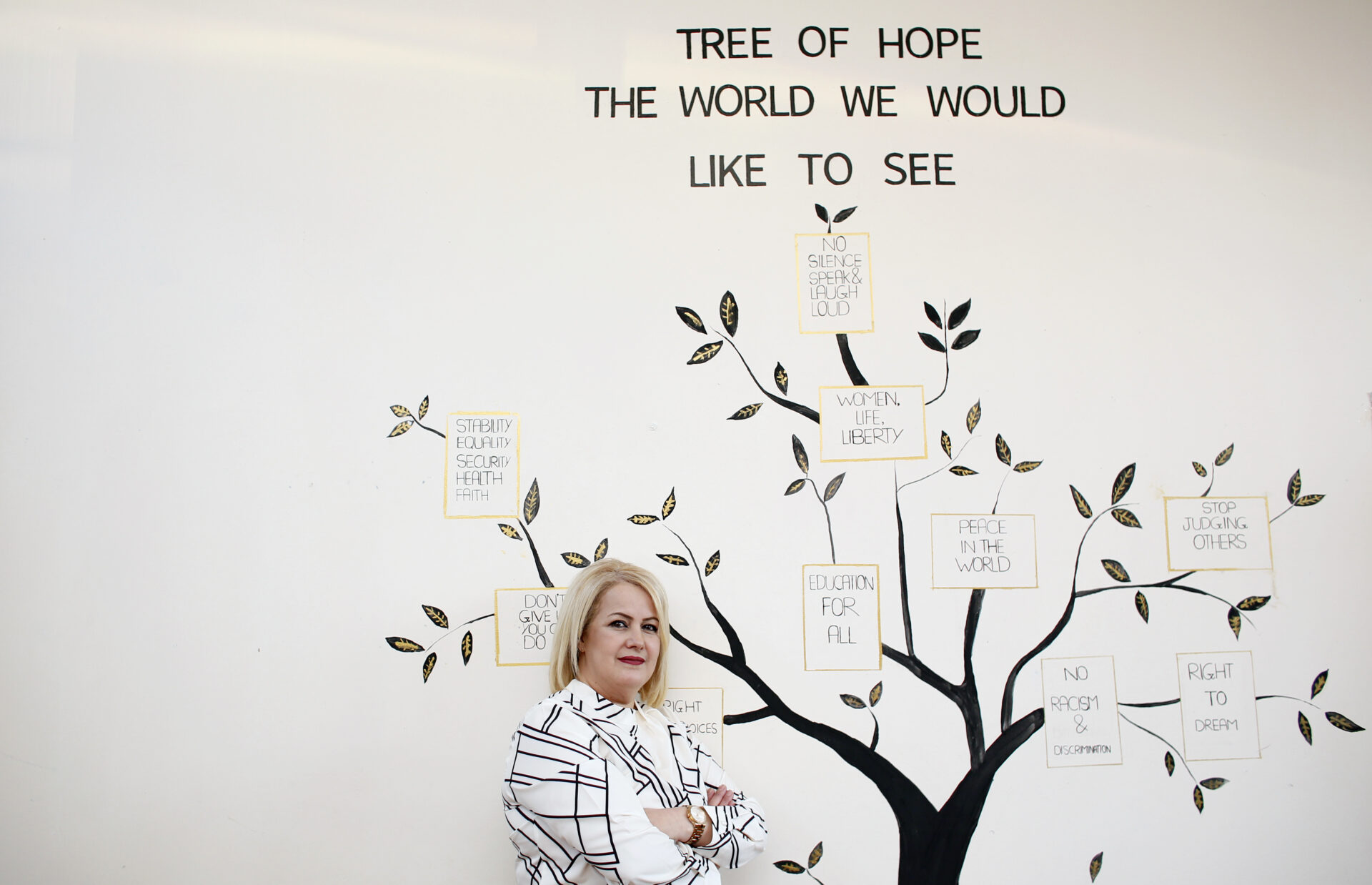 Article: Torture charity calls for governments to better protect women from violence Image description: Ahlam Souidi, a community development worker with Freedom from Torture, in Glasgow, standing confidently in front of a painted mural that reads, “TREE OF HOPE: THE WORLD WE WOULD LIKE TO SEE.”